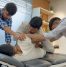 A team of three physiotherapists working together to perform advanced manual therapy on a patient lying on a treatment table in a modern clinic. The therapists are focused on adjusting the patient's upper body and hip area to improve mobility and relieve pain.