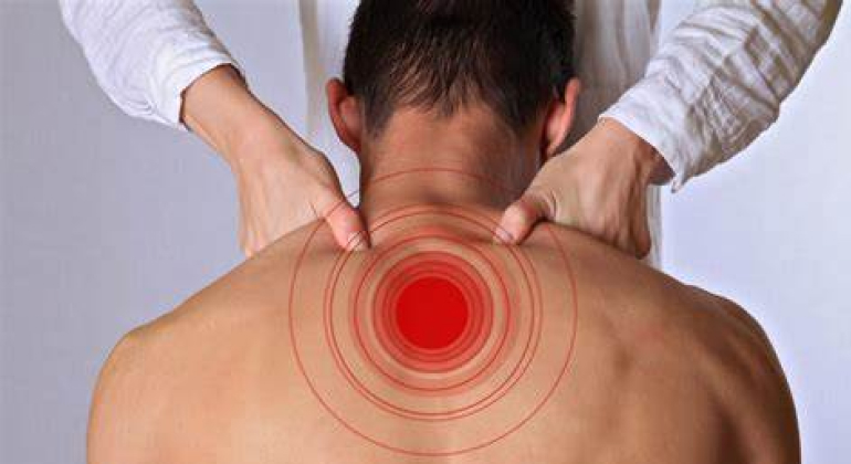 A person receiving a shoulder massage, with red concentric circles indicating a pain point on their upper back. The hands of the therapist are applying pressure to the affected area to relieve pain and tension. The image highlights the focus on pain relief through physiotherapy techniques.