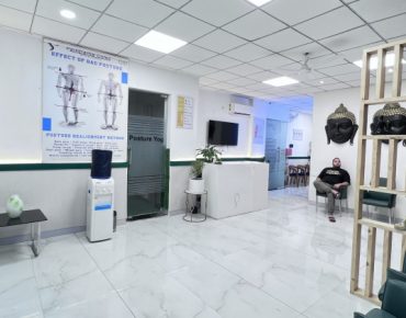 A modern physiotherapy clinic in Gurugram featuring a clean and spacious waiting area with comfortable seating. The decor includes educational posters on posture, Buddha sculptures, and a partition with plants. A patient is seated in the waiting area, creating a serene and welcoming atmosphere.
