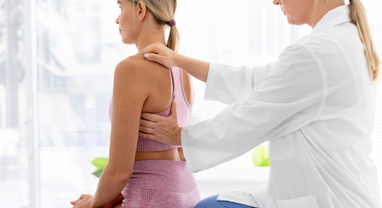 Doctor examining a patient's back posture in a medical office.