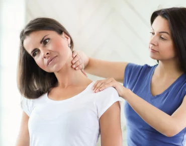 Therapist applying pressure to a patient's neck and shoulder area to relieve trigger points in a bright, modern setting