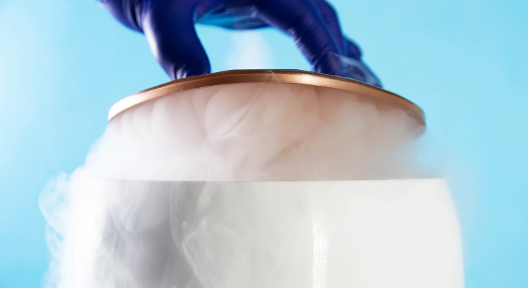 A gloved hand handling a container with cold vapor rising from it, representing the use of liquid nitrogen in cryotherapy.