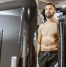 The image shows a man undergoing a whole-body cryotherapy session. He is standing inside a cryotherapy chamber, with the top half of his body exposed while the lower half is enclosed within the chamber. The man is wearing black shorts and appears calm and focused as he experiences the extreme cold temperatures used in cryotherapy. The chamber is sleek and modern, equipped with control panels and displays, highlighting the advanced technology used in cryotherapy treatments. This image captures the process of cryotherapy, emphasizing its role in wellness and recovery therapies.