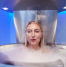 Person undergoing a cryotherapy session inside a chamber, with cold mist surrounding them in a blue-lit room.