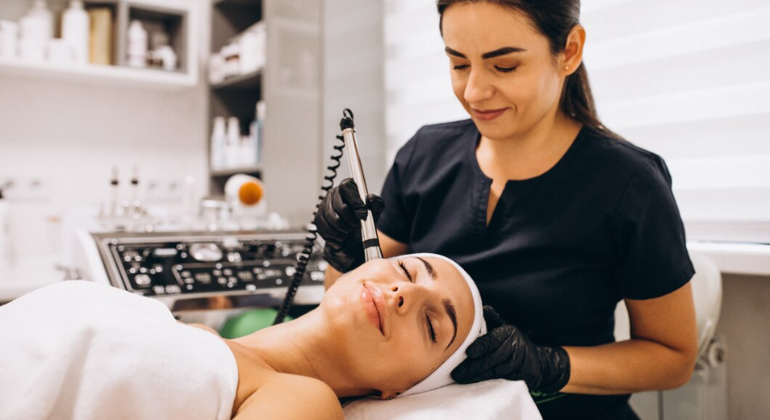 A smiling therapist performing a relaxing cryofacial treatment on a woman in a clinic, with specialized equipment in use and the patient looking calm and content.