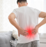 Man holding his lower back in pain, with a red highlighted area to indicate the location of discomfort, standing in a home environment. The image symbolizes chronic pain, possibly related to conditions like back pain or muscle strain.