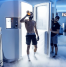 An athlete steps out of a cryotherapy chamber surrounded by cold vapor, wearing protective gloves and drinking from a bottle post-session. A technician assists nearby, with nitrogen tanks visible in the background used to cool the chamber for whole-body cryotherapy.