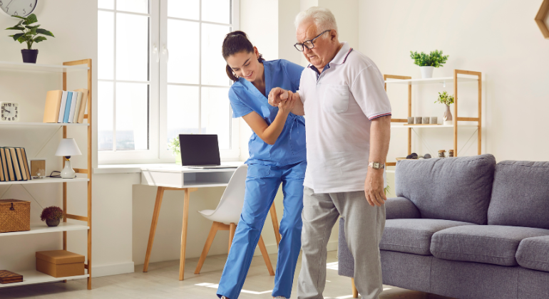 Physiotherapist assisting an elderly man with walking exercises during a home-based rehabilitation session to improve mobility and balance.