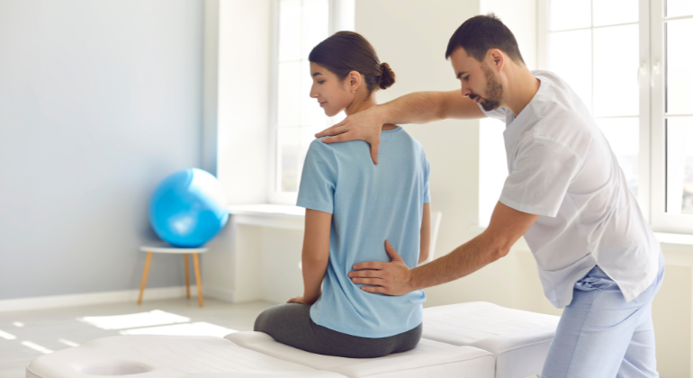 Physiotherapist performing back adjustment on a female patient during a rehabilitation session in a clinic setting.