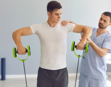 Physiotherapist guiding a male athlete through shoulder rehabilitation exercises using resistance bands during a sports injury recovery session.