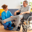 Physiotherapist helping an elderly man in a wheelchair with leg mobility exercises during a home physiotherapy session in a warm, well-lit living space.