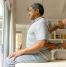 Physiotherapist performing back therapy on an elderly man during a home physiotherapy session in a bright, comfortable living space.