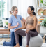 Physiotherapist guiding a pregnant woman through stability exercises using an exercise ball during a home physiotherapy session in a cozy, well-lit living space.