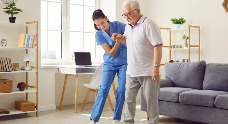 Physiotherapist assisting an elderly man with mobility exercises during a home physiotherapy session in a cozy and well-lit living room