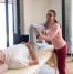 Physiotherapist assisting an elderly man with leg mobility exercises during a home physiotherapy session in a bright, spacious room with natural light.