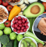 A variety of healthy, nutrient-rich foods such as fruits, vegetables, nuts, and seeds alongside an image of a person holding their abdomen, symbolizing the role of diet in navel displacement recovery.