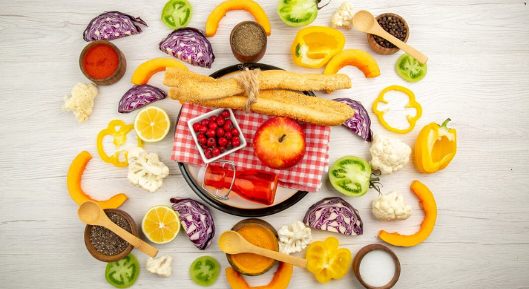 A vibrant display of healthy foods, including colorful vegetables, fruits, spices, and grains arranged around a plate with breadsticks, apple, and cranberries. The image emphasizes the importance of a balanced diet for overall health and recovery.