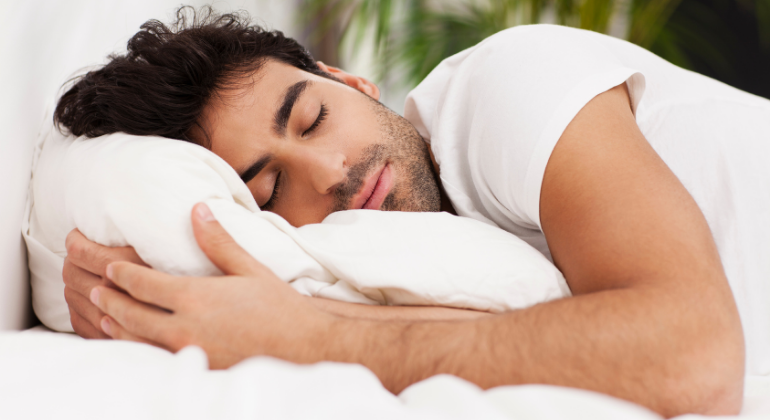 A man sleeping peacefully on his side, resting his head on a soft pillow, appearing relaxed and comfortable.