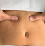 A close-up image of a person receiving an abdominal massage, with fingers applying pressure around the navel, possibly for navel realignment or relief from discomfort.