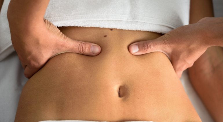 A close-up image of a person receiving an abdominal massage, with fingers applying pressure around the navel, possibly for navel realignment or relief from discomfort.