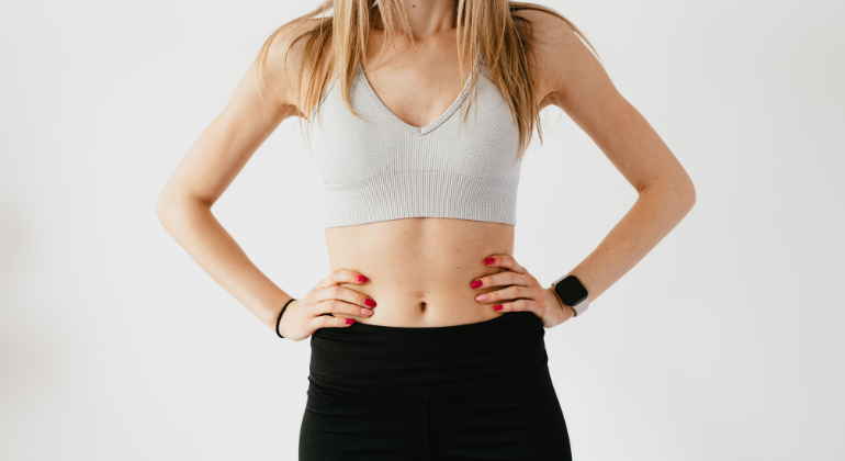 A fit woman in athletic wear standing with her hands on her waist, highlighting a strong core and abdominal area, possibly representing fitness, core strength, or digestive health.